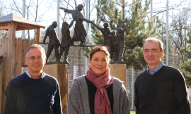 Pater Rainer Reitmaier, Julia Dahmen und P. Clemens Mörmann stehen vor einer Statue von Don Bosco, der über einen von Erwachsenen und Jugendlichen gehaltenen Balken balanciert.