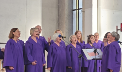 11 Mitglieder des Chors Don Bosco Gospel & Joy singen in lilanen Gewändern.